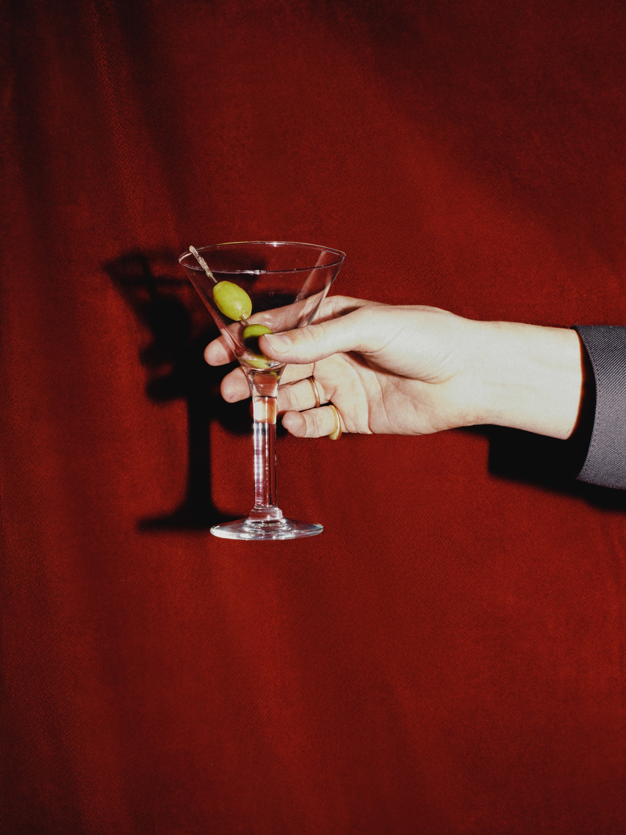 Hand hält einen Martini vor rotem Hintergrund